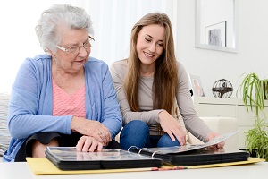 old senior woman with young granddaughter at home looking at memory in family photo album