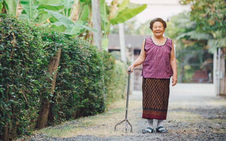 Senior woman walking with a cane through a gravel alley