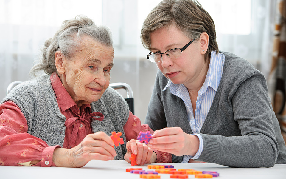 Senior woman with dementia doing a puzzle with her elder care nurse